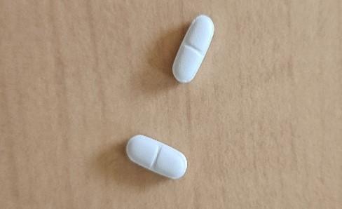 2 comprimés (médicaments) posés sur une table en bois