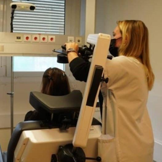une personne est vue de profil, un appareil en forme de huit posée sur le front. En arrière plan, un écran avec une image d'IRM de cerveau